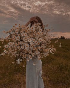 a woman standing in a field holding a bouquet of daisies up to her face