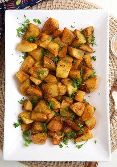 a white plate topped with potatoes and parsley on top of a woven place mat