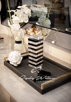 a black and white tray with flowers on it next to a glass vase filled with water