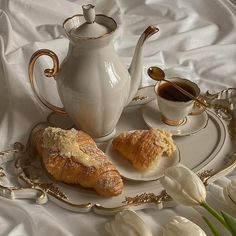 two croissants on a plate next to a tea pot