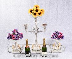 three bottles of champagne and two vases with flowers on them sitting on a silver tray