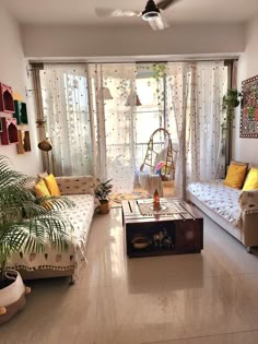 a living room filled with furniture and lots of plants in front of a window covered by curtains