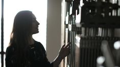 a woman standing in front of a window looking at something on the wall behind her