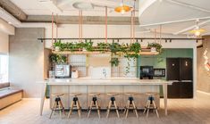 an open kitchen with plants hanging from the ceiling and bar stools in front of it