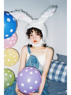 a woman with bunny ears holding balloons in front of her face and wearing overalls