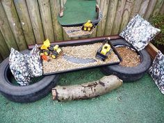 an outdoor play area with tires, gravel and toys in the ground next to a wooden fence