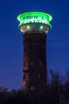 a tall tower with a neon green sign on it's top at night time