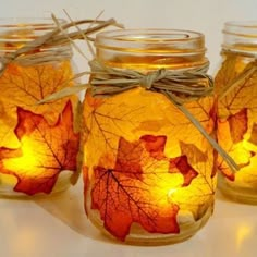 three mason jars filled with autumn leaves and twine tied to the lids, all lit up