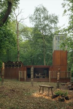 a wooden cabin in the woods with picnic table and benches on the grass near it