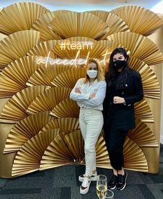 two women standing next to each other in front of a gold wall with words on it