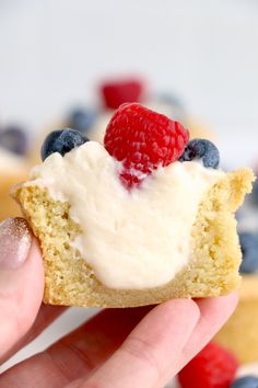 a hand holding a piece of cake with cream and berries on top