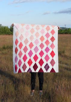 a person standing in a field holding up a quilt