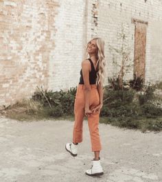 a woman standing in front of a brick building wearing an orange jumpsuit and white sneakers