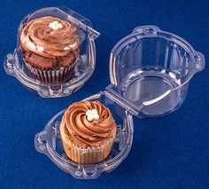 three cupcakes with chocolate frosting in plastic cases on a blue tablecloth