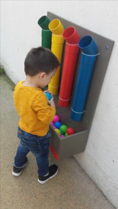 a little boy playing with some colorful plastic balls in front of a wall mounted art piece