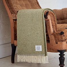 a brown chair with a green and white blanket on it's back next to a wall