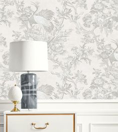 a white lamp sitting on top of a dresser next to a wallpapered wall