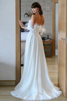 a woman in a white dress is looking at her reflection in the mirror while standing next to an open door