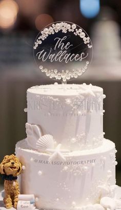 a white wedding cake with a teddy bear on top and an acrylic sign that says the wallaces