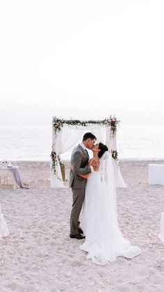 a bride and groom kissing on the beach in front of their wedding ceremony arch decorated with flowers