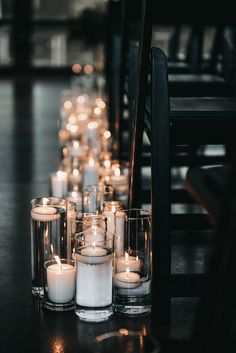 many lit candles are lined up on the floor next to each other in glass vases