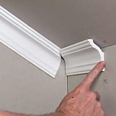 a person pointing at the corner of a wall with white molding on it's edge