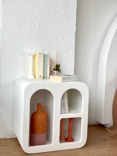 a white shelf with two orange vases and books on it next to a wall