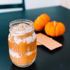 an orange and white dessert in a glass jar on a table next to some pumpkins