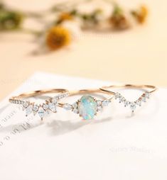 three rings with opal and diamonds on top of a piece of paper next to flowers