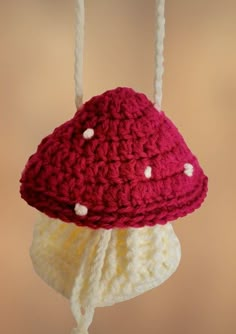 a crocheted hat hanging from a hook on a string with two white strings