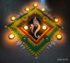 a decorated diya with lit candles on the floor in front of it and an image of lord ganeshh