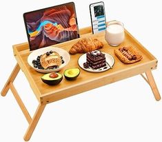 a wooden tray with food on it next to a cell phone and laptop computer screen