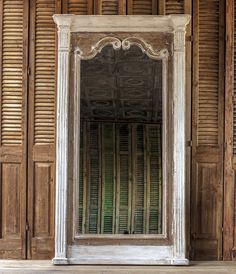 an old white mirror sitting on top of a wooden floor next to a wall covered in shutters