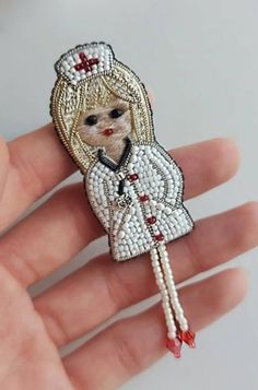 a hand holding a white and red beaded doll brooch