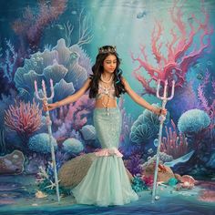 a woman dressed in a mermaid costume holding two scallops and standing on the ocean floor