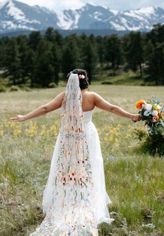 a woman in a wedding dress holding her arms out to the side with mountains in the background