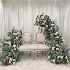 two white chairs sitting next to each other in front of a wall with flowers on it