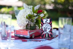 the table is set with red and white flowers in vases, books, and cards