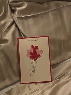 there is a card with some hearts on it sitting on the bed sheet that's covered in satin material