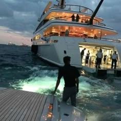 a man standing on top of a boat in the ocean next to another boat at night