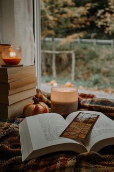 an open book sitting on top of a bed next to a candle and some books