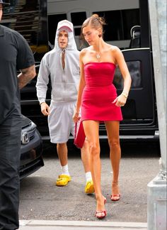 a woman in a red dress is walking down the street with a man behind her