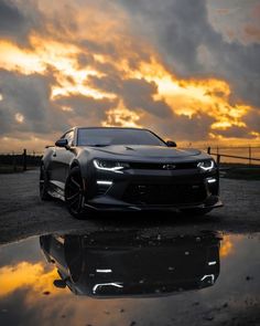 a chevrolet camaro is parked in front of a sunset with clouds reflecting on the ground