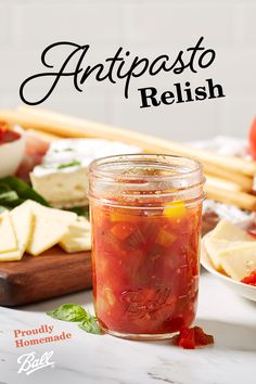 a glass jar filled with tomato relish sitting on top of a table next to cheese and bread