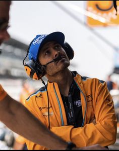 a man wearing a helmet and ear muffs is talking to another man in the background