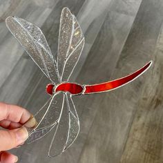 a hand holding a piece of glass that looks like a dragonfly with red wings