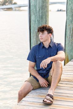 a young man sitting on a dock next to the water