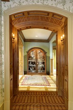 an ornate entry way with wooden doors and tile flooring in the hallway, leading to another room