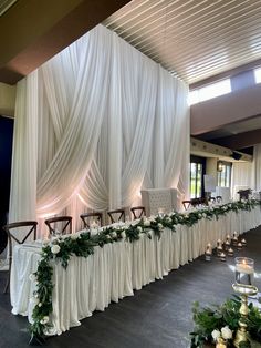 a long table covered in white cloths and greenery