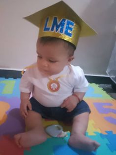 a baby sitting on the floor wearing a graduation hat that says l m e in blue and gold